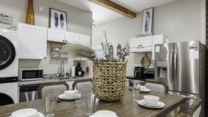 Une cuisine moderne avec des meubles blancs, des appareils en acier inoxydable et une table à manger en bois pour quatre personnes.