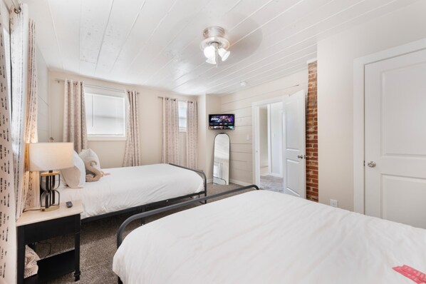Een hotelkamer met twee bedden, een televisie, een spiegel en een deur naar een andere kamer.