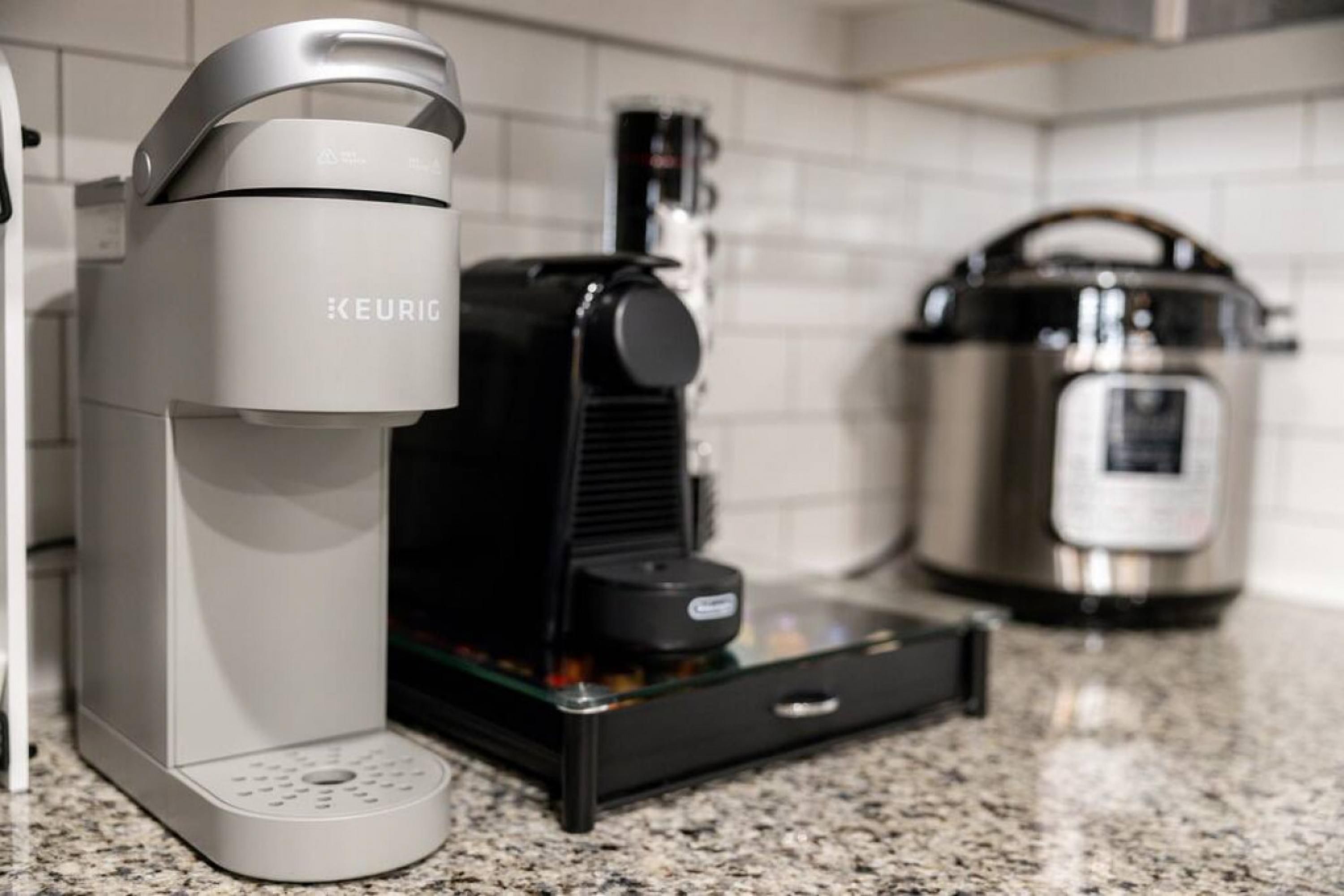 Eine Küche mit einer Keurig-Kaffeemaschine, einer schwarzen Kaffeemaschine und einem Edelstahl-Slowcooker.