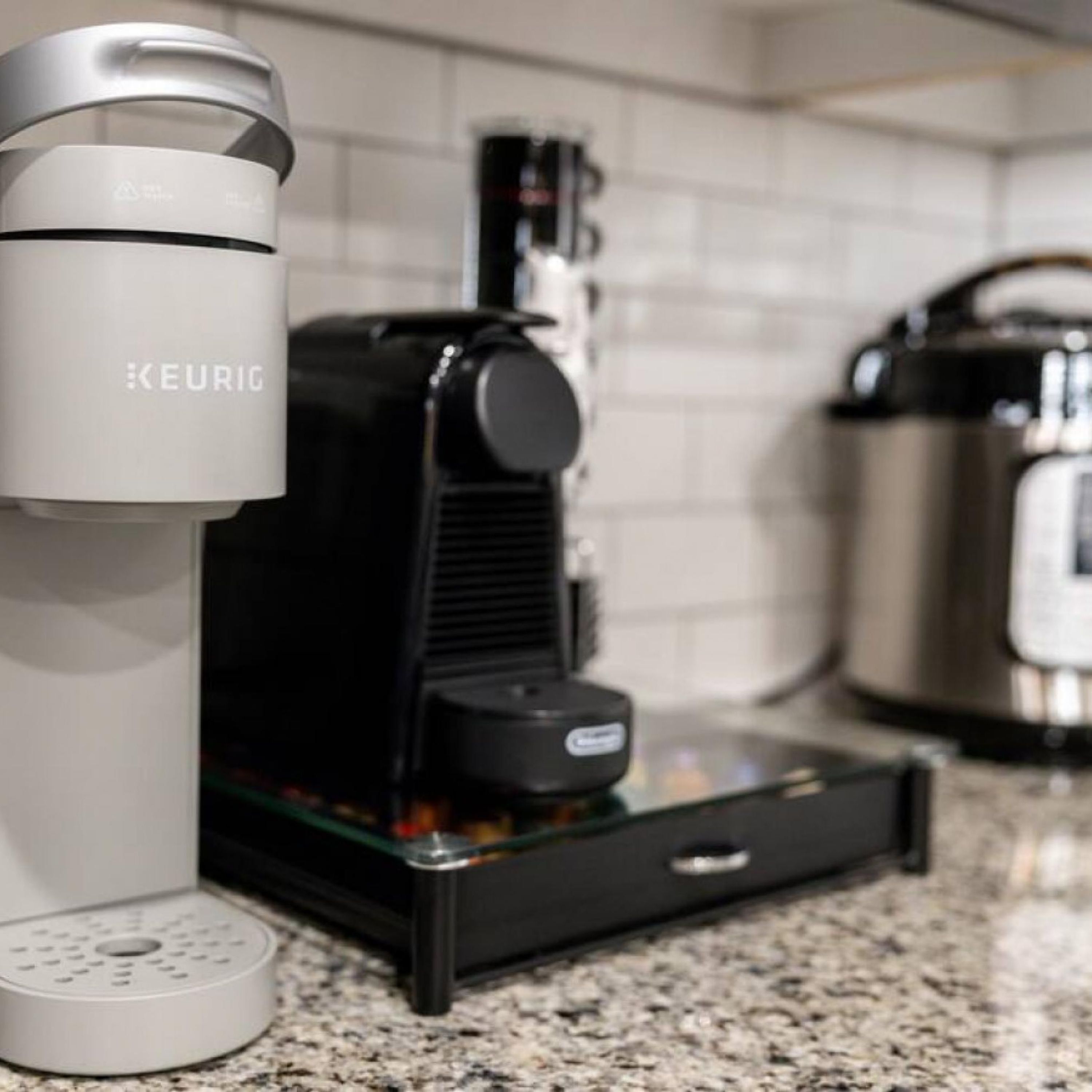 Una cafetera Keurig sobre una encimera de cocina, con un porta cápsulas de café y una jarra de café al fondo.