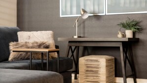 Ein modernes Wohnzimmer mit einem dunklen Sofa, einem kleinen Holztisch, einer Lampe und einem Blumentopf.