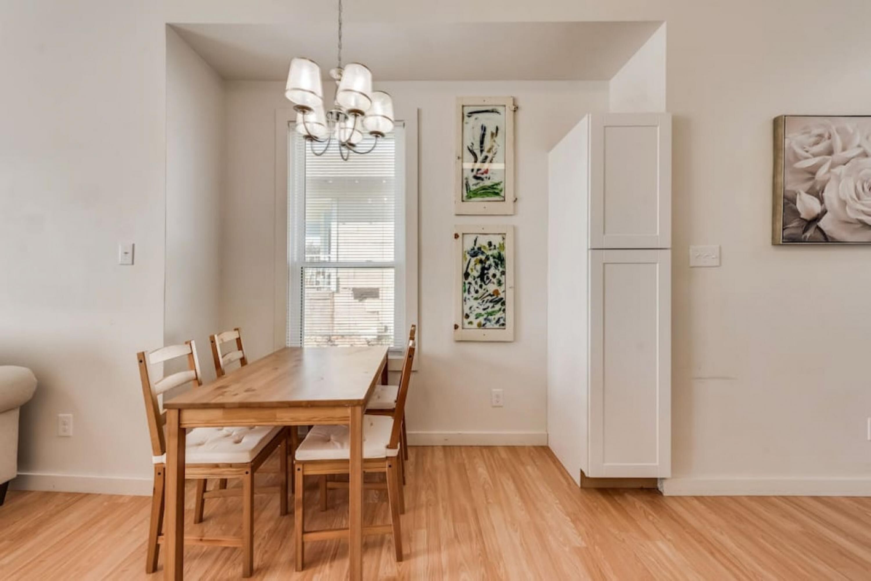 Een eetruimte met een houten tafel en stoelen, een kroonluchter en kunstwerken aan de muur.