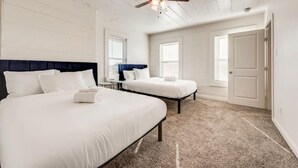 Une chambre avec deux lits, un ventilateur de plafond et une grande fenêtre.
