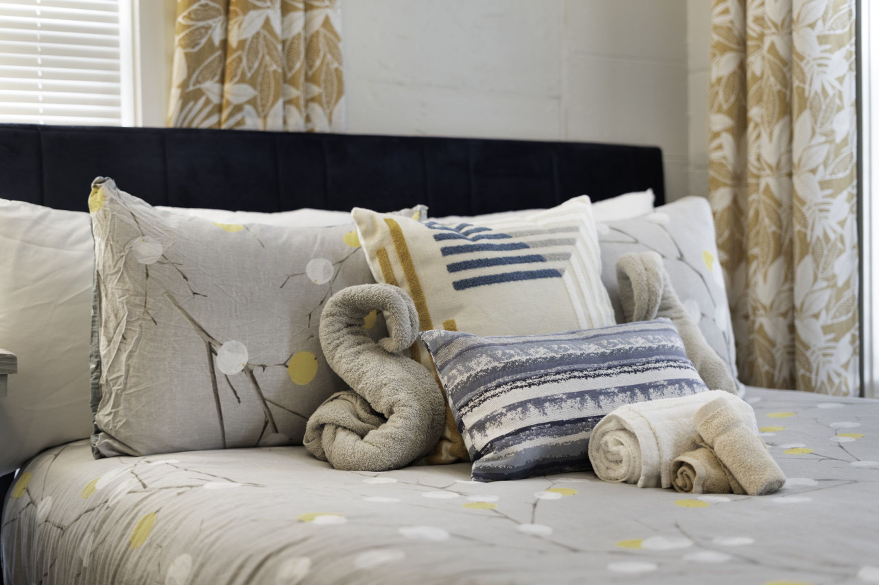 Un lit bien fait, avec une couvre-lit à motifs, une serviette enroulée et un coussin décoratif.