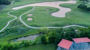 Vue aérienne d’un terrain de golf avec des bunkers de sable, des obstacles d’eau et un bâtiment au toit rouge.