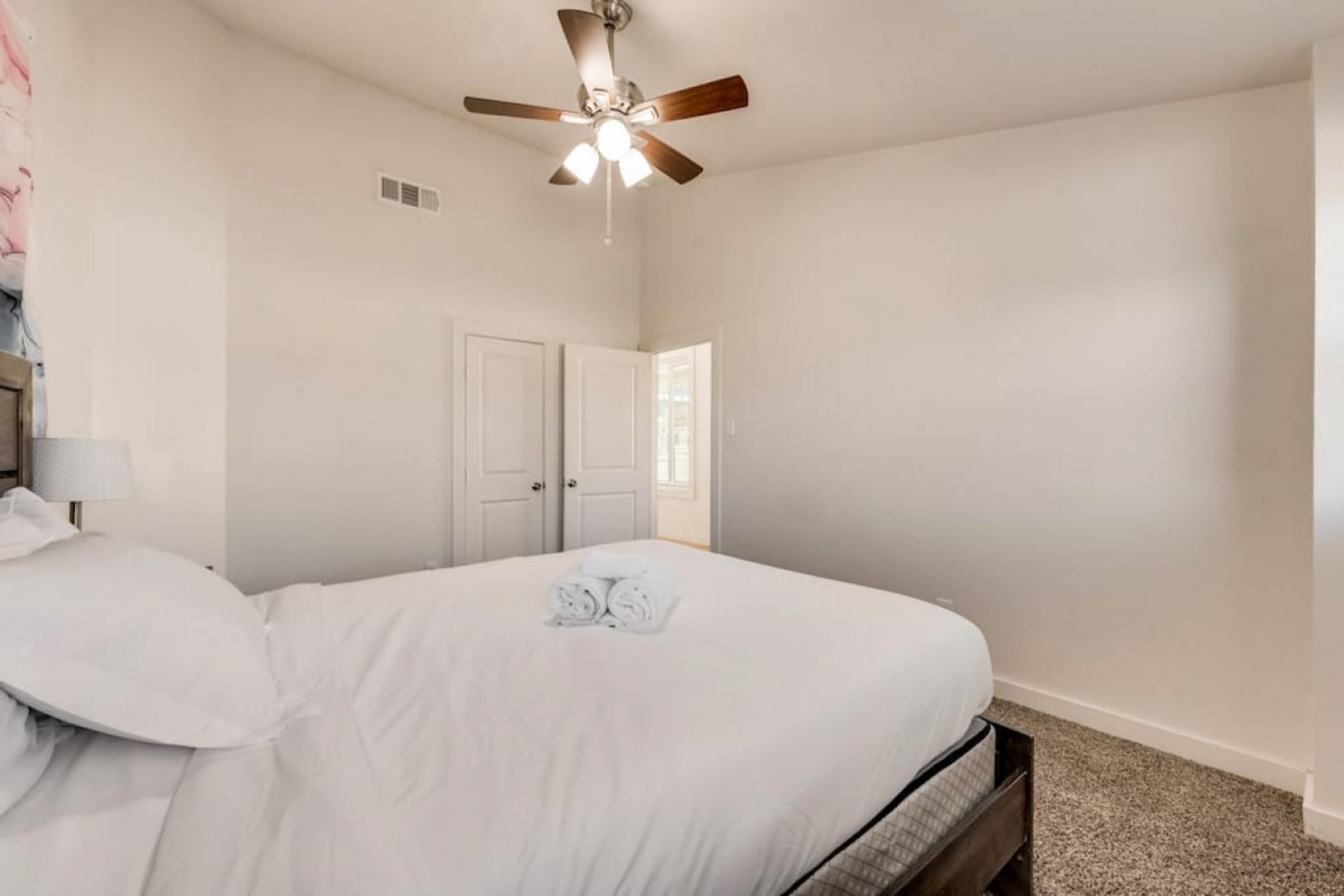 A bedroom with a bed, a ceiling fan, and a door.