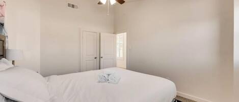 A bedroom with a bed, a ceiling fan, and a door.