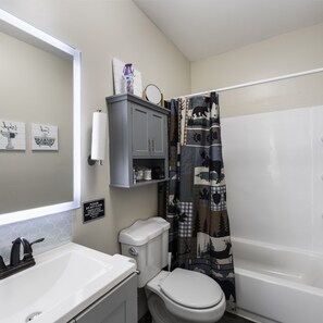 A bathroom with a white sink, toilet, and bathtub. There is a cabinet above the toilet and a sign on the wall. - 4 Queen Beds High Speed Wifi (Fort Worth)