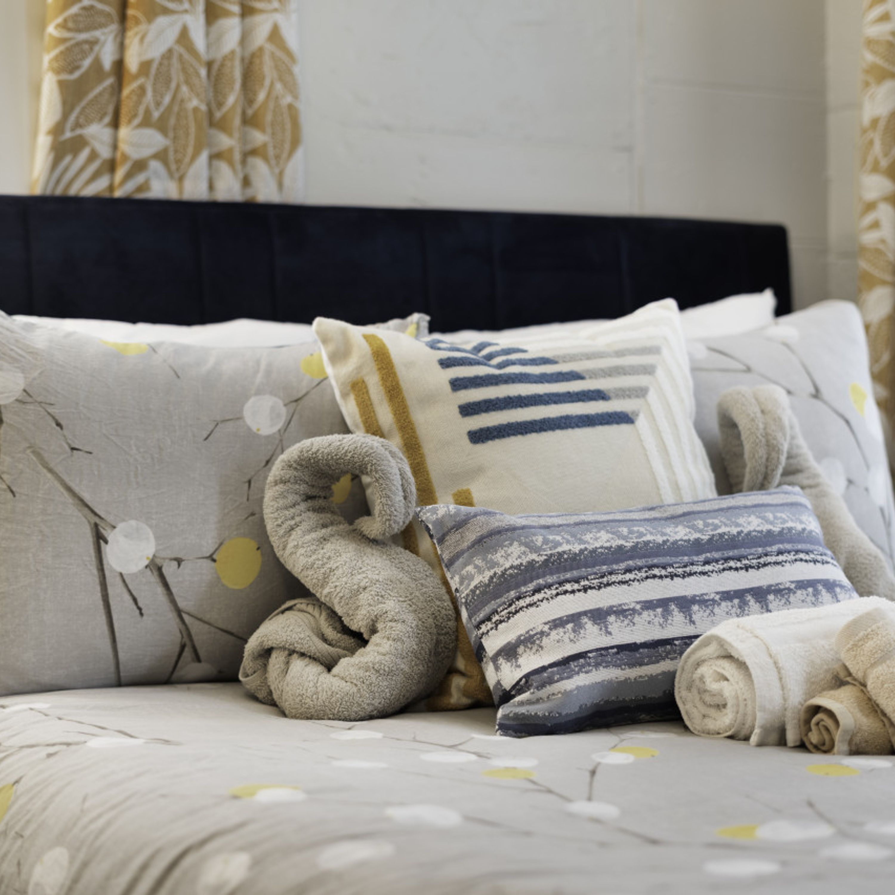 A bed with a patterned bedspread, multiple pillows, and a rolled-up blanket.
