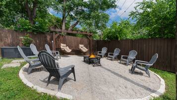 A backyard with a fire pit, outdoor seating, and a wooden pergola.