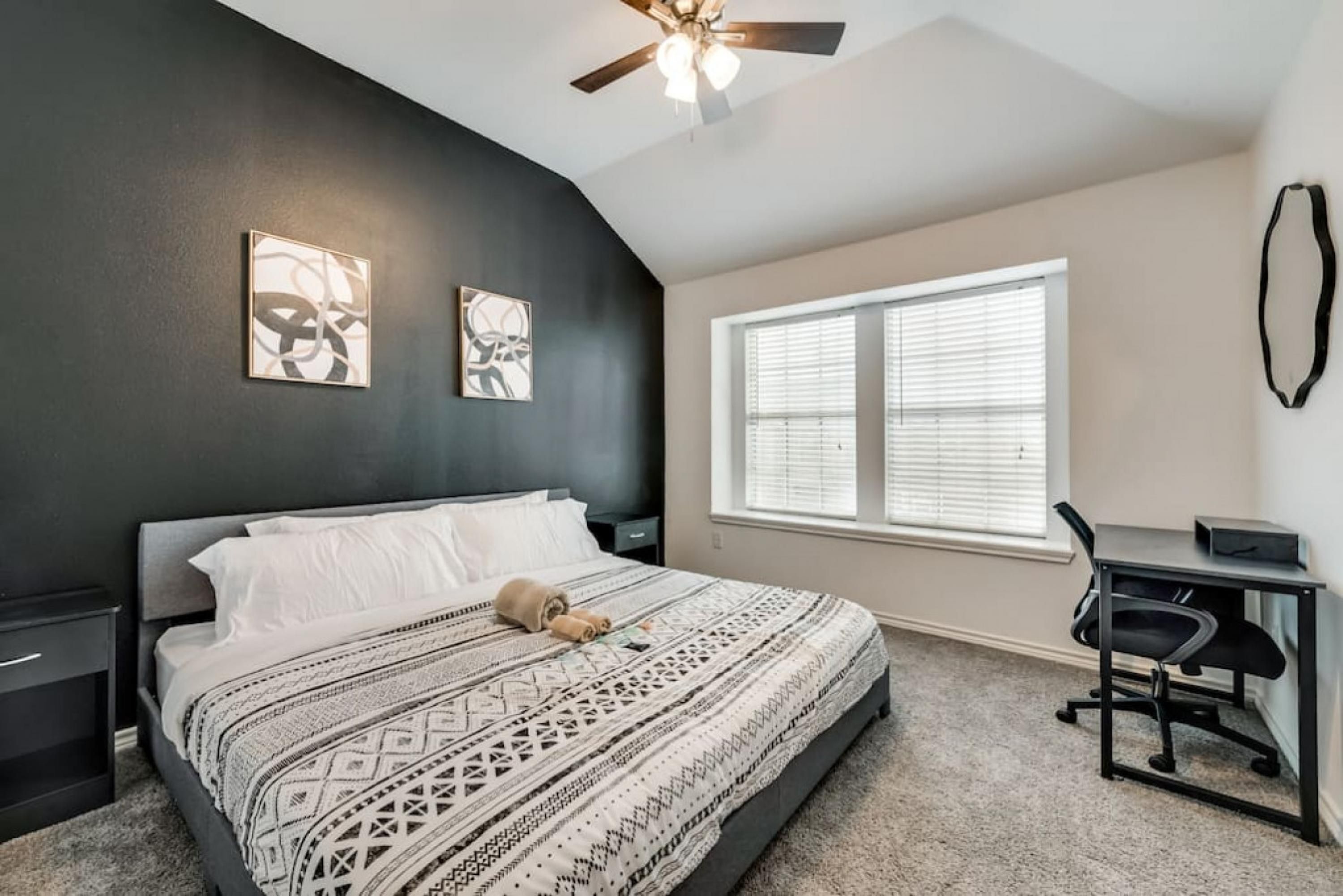 A bedroom with a bed, a desk, a chair, a ceiling fan, and a window with blinds.