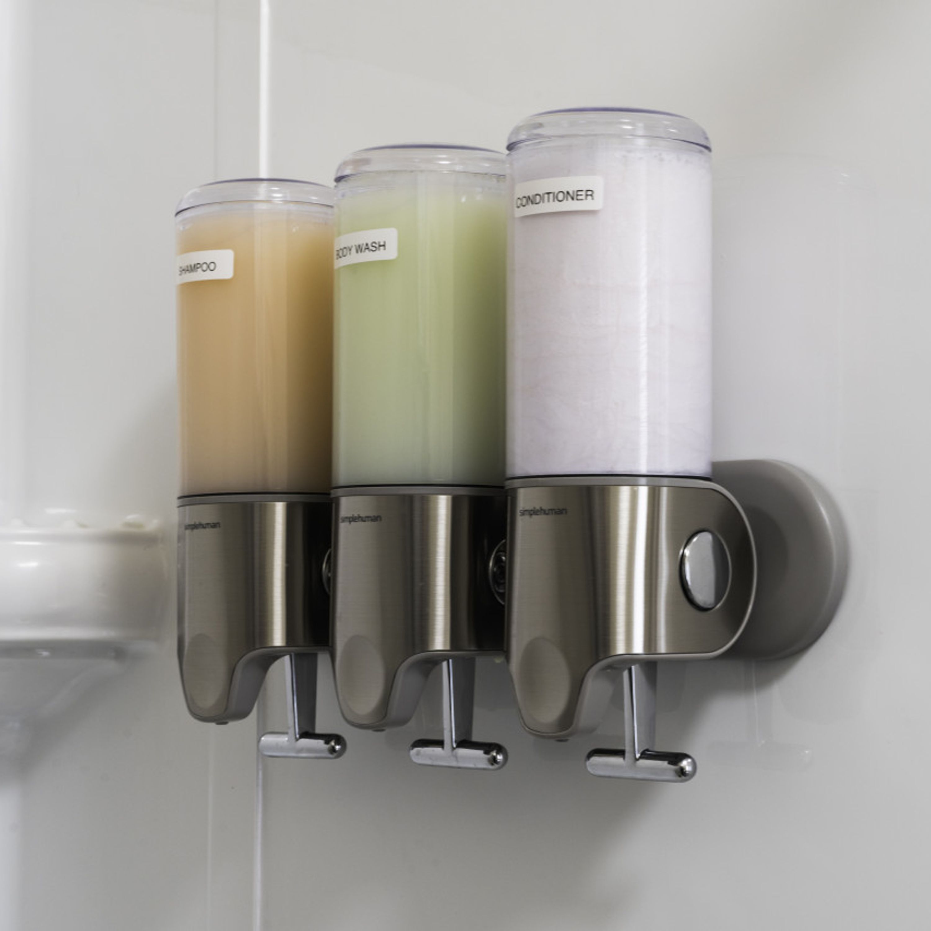 Un distributeur mural doté de trois compartiments étiquetés « shampoing », « gel douche » et « après-shampoing ».