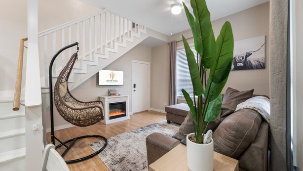 Un salon moderne avec un escalier blanc, un fauteuil suspendu, une cheminée, un canapé et une grande plante.