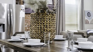 Une table à manger dressée avec de l’assiette blanche, des bols et de la verrerie transparente, agrémentée d’un centre de table en forme de panier tressé.