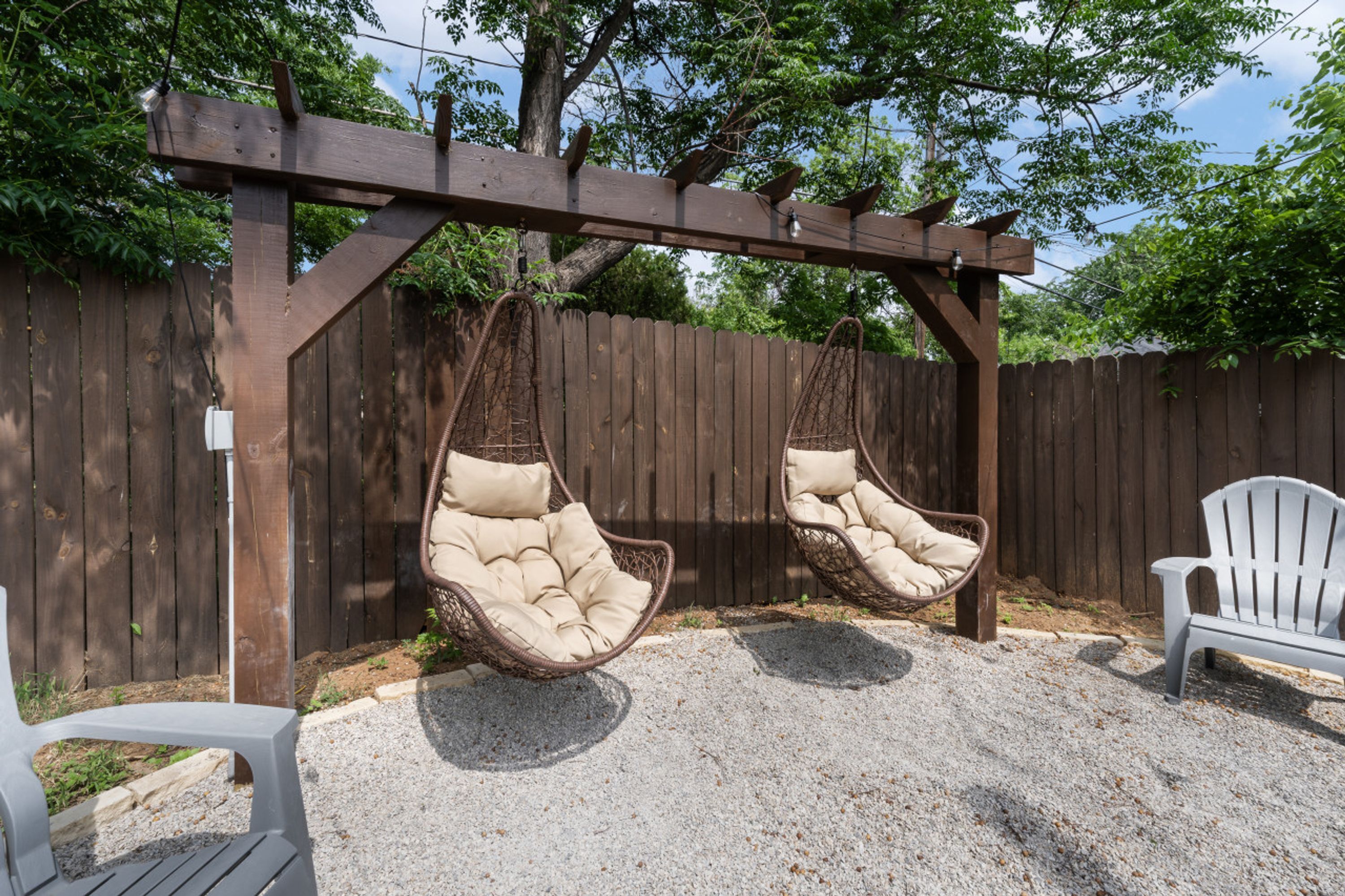 A wooden pergola with two hanging chairs and a white chair in a garden area.