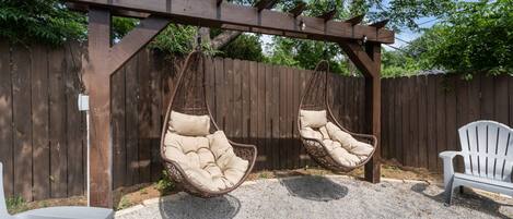 A wooden pergola with two hanging chairs and a white chair in a garden area.