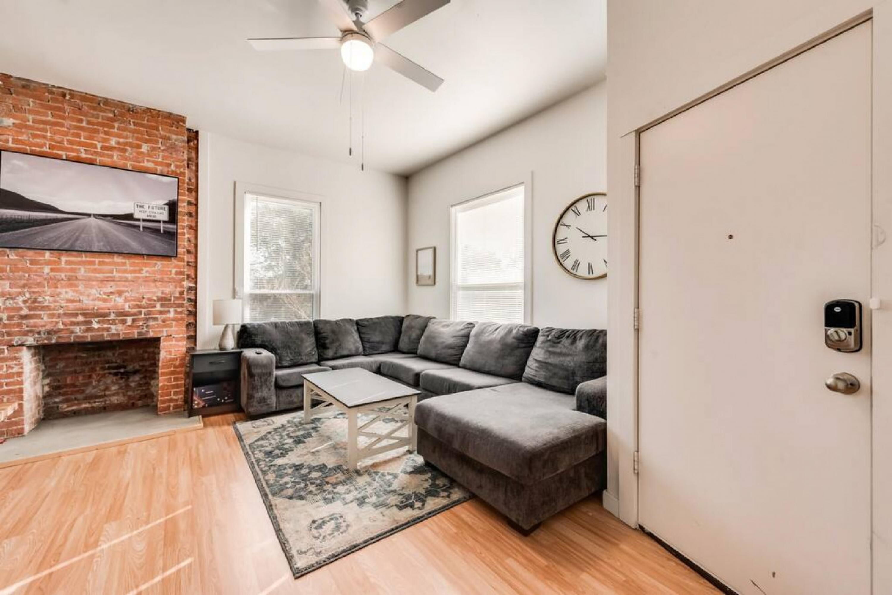 A living room with a brick fireplace, a sectional sofa, a coffee table, and a rug.