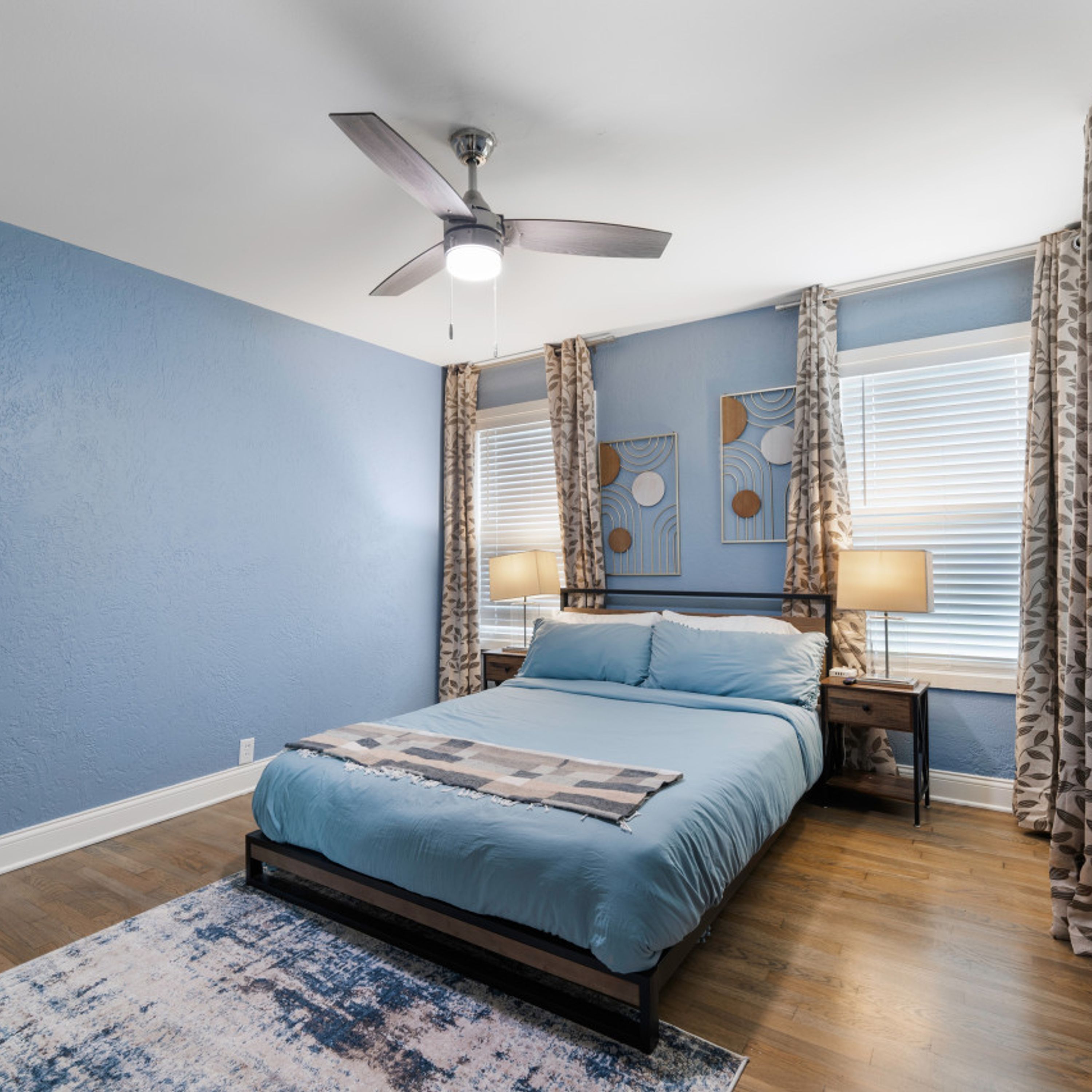 A bedroom with a bed, two bedside tables, a ceiling fan, and a window with curtains.