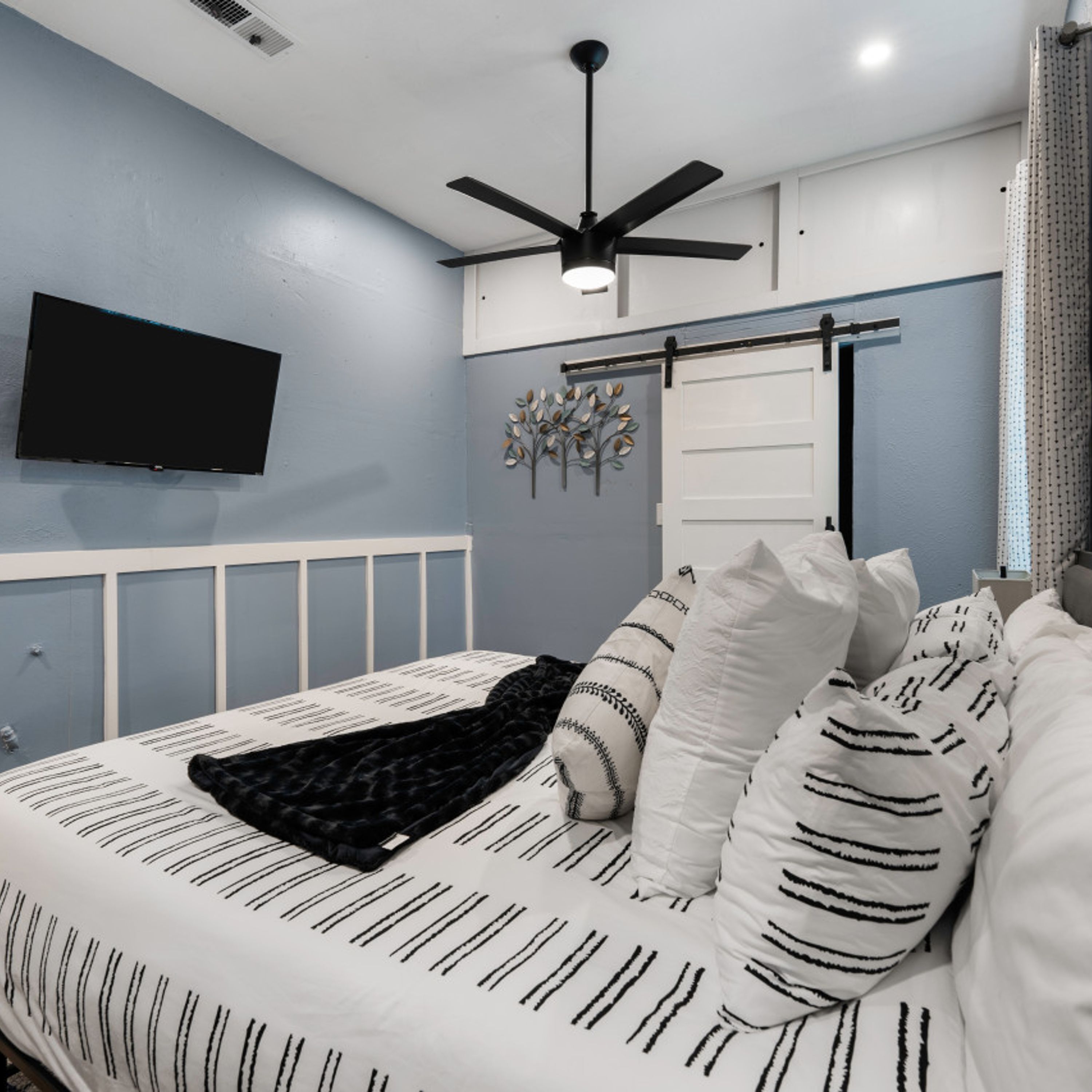 Ein Schlafzimmer mit Bett, Deckenventilator, angebrachtem Fernseher und Wandradiator.
