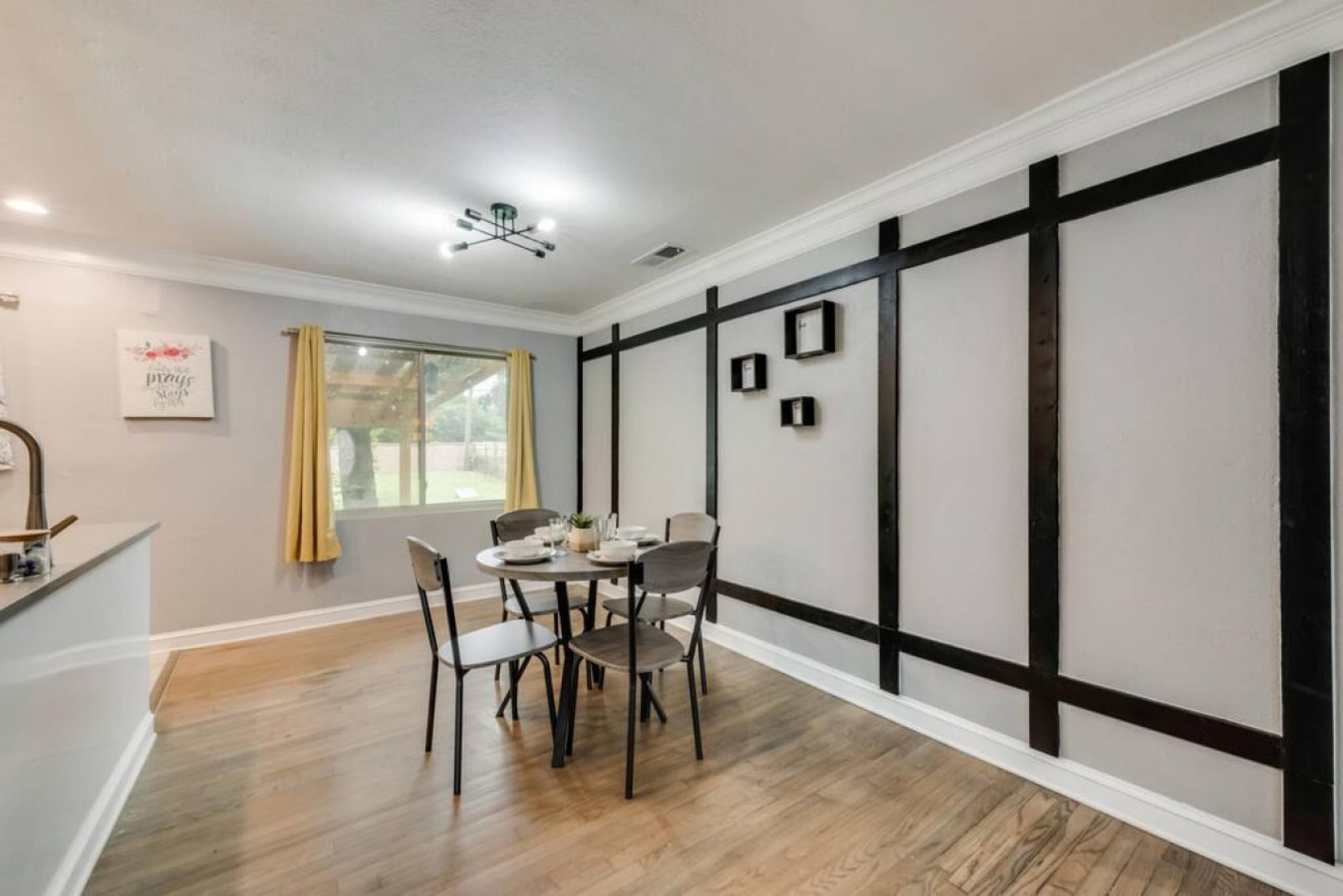Un coin repas avec une table ronde et des chaises, une fenêtre avec des rideaux et un mur recouvert de panneaux noirs et blancs.
