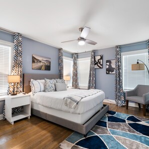 A bedroom with a bed, nightstands, a chair, patterned curtains, and artwork on the walls. - Rare Exclusive Retreat Private Hot Tub King Bed (Arlington)