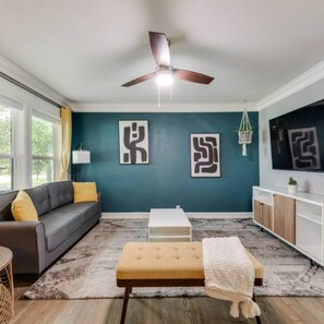 A modern living room with a grey sofa, a white coffee table, and a beige bench. There are abstract wall art pieces and a ceiling fan. - Rare Exclusive Retreat Private Hot Tub King Bed (Arlington)
