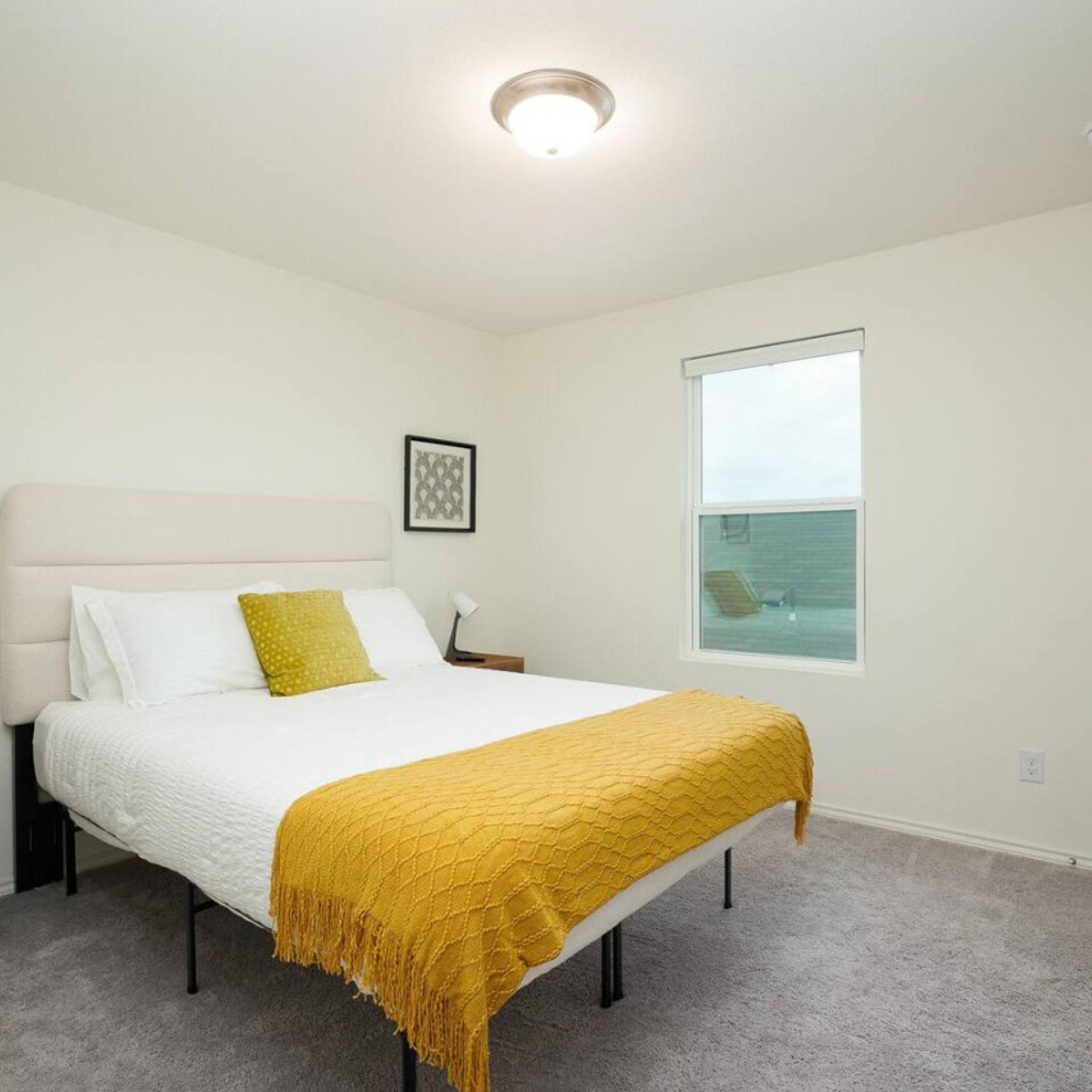 A bedroom with a bed, a nightstand, a framed picture, and a window.