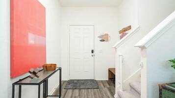 A hallway with a white door, a red accent wall, a black console table with a wooden bowl, and a grey rug.
