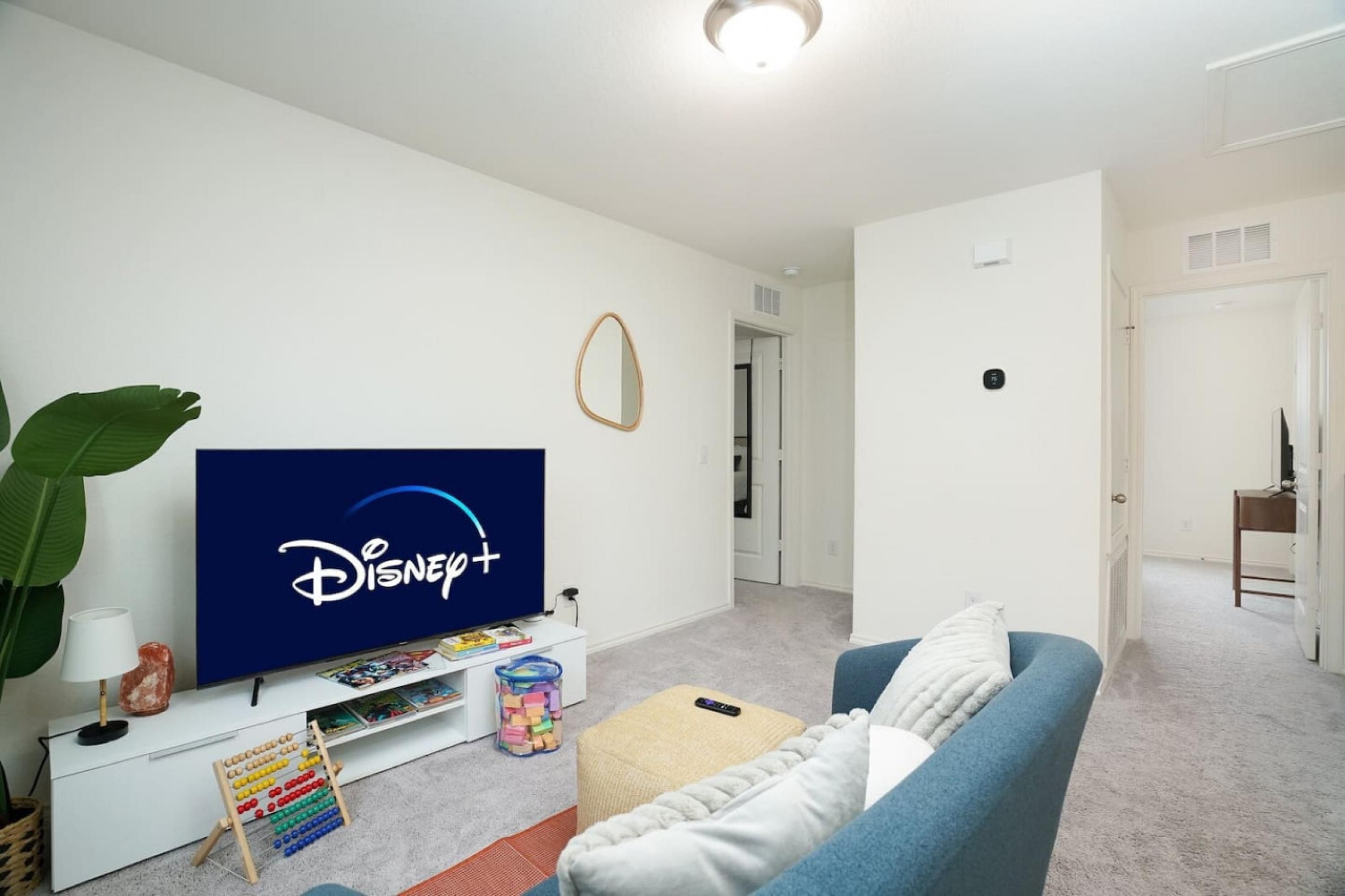 A living room with a flat-screen TV, a blue couch, a small table, and a plant.