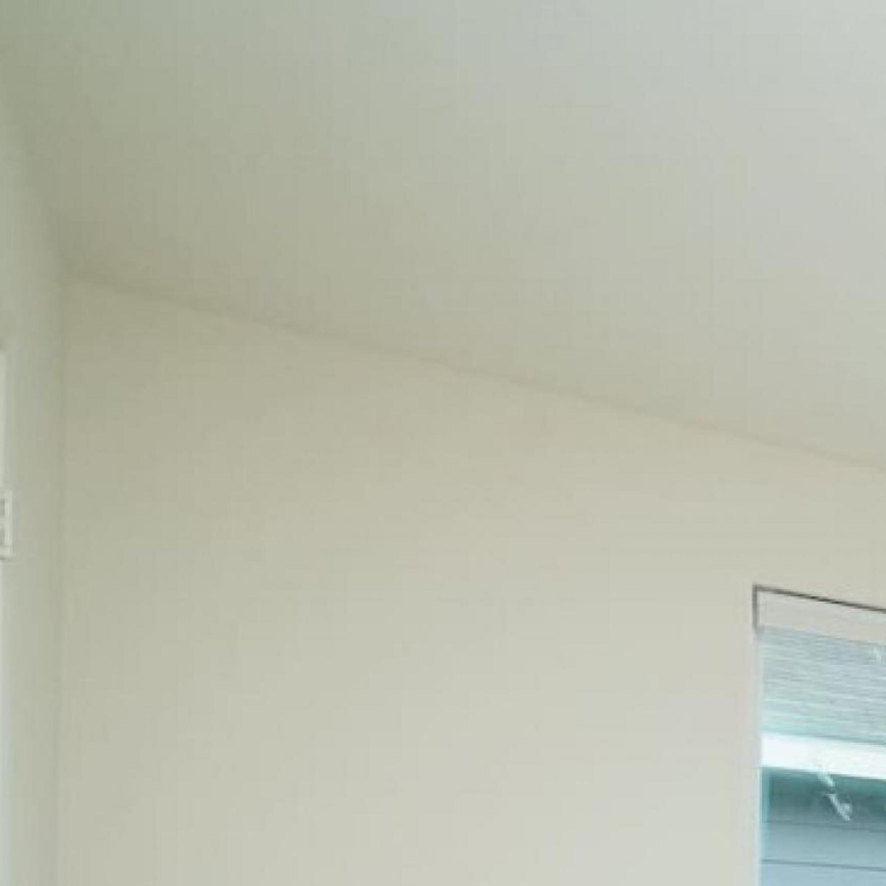 Ein Zimmer mit großem Fenster, weißen Wänden und einer Tür.
