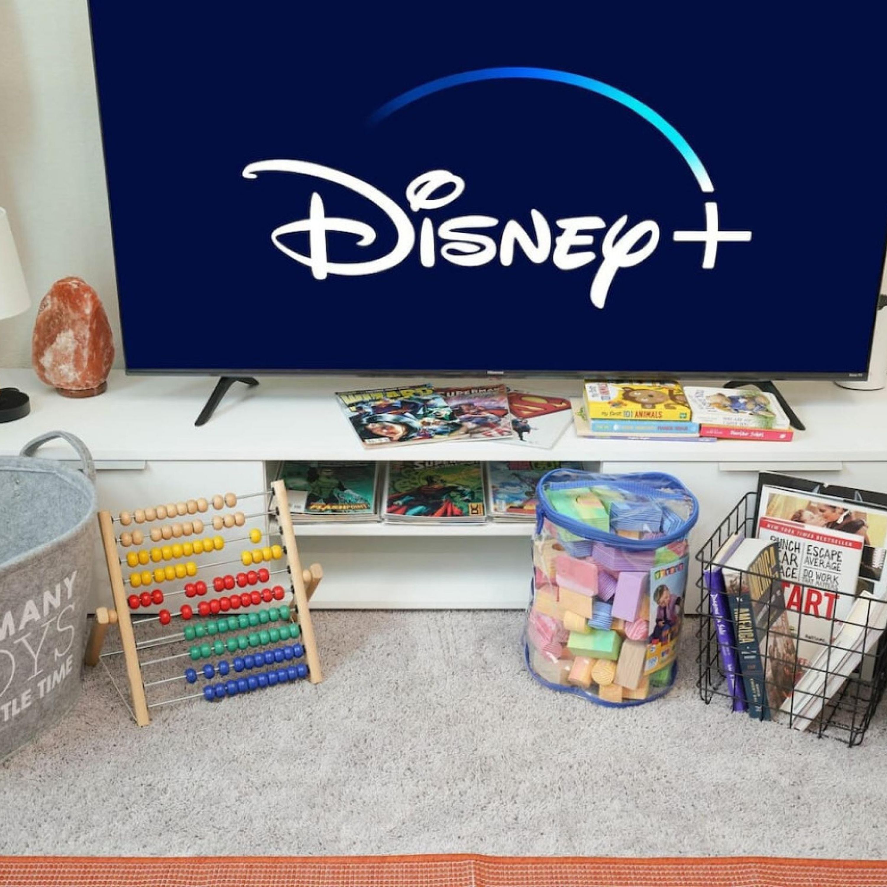Ein Zimmer mit einem Fernseher, der das Disney+-Logo zeigt, einem Bücherregal mit Kinderbüchern, einem bunten Rechenrahmen und einer Aufbewahrungsbox mit Spielzeug.