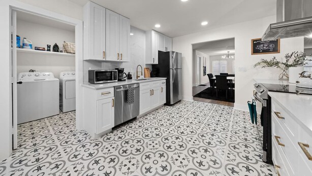 Una cocina moderna con armarios blancos, electrodomésticos de acero inoxidable y baldosas de piso estampadas.