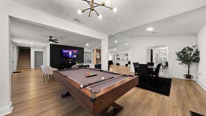 Una sala de estar moderna con mesa de billar, televisor de pantalla plana y comedor con mesa y sillas negras.