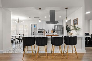 Una cocina moderna con armarios blancos, un refrigerador de acero inoxidable e una isla central con taburetes de bar.