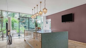 A modern kitchen with a granite island, pendant lights, and a large window offering a view of greenery. - Art Deco Villa Oxford (Oxford)