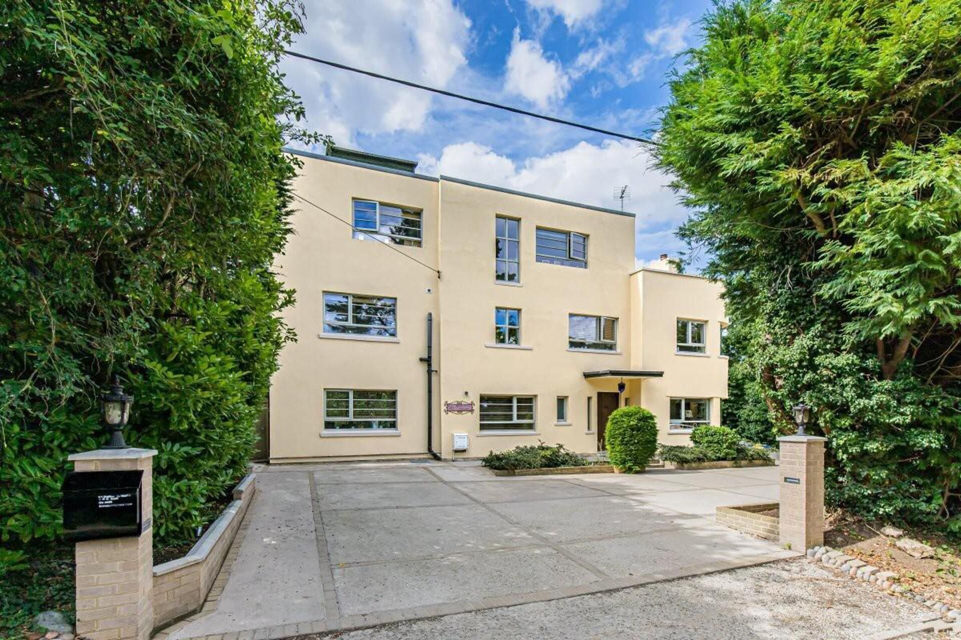 A two-story building with a beige facade, multiple windows, and a small front garden.