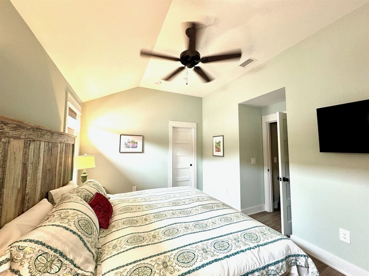 Une chambre à coucher avec un lit, un ventilateur de plafond, une porte et un téléviseur fixé au mur.