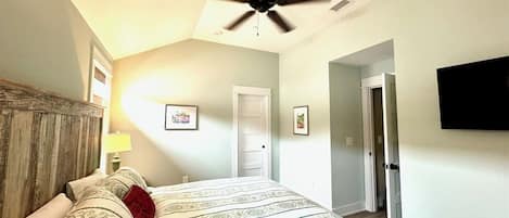 A bedroom with a bed, a ceiling fan, a door, and a wall-mounted TV.