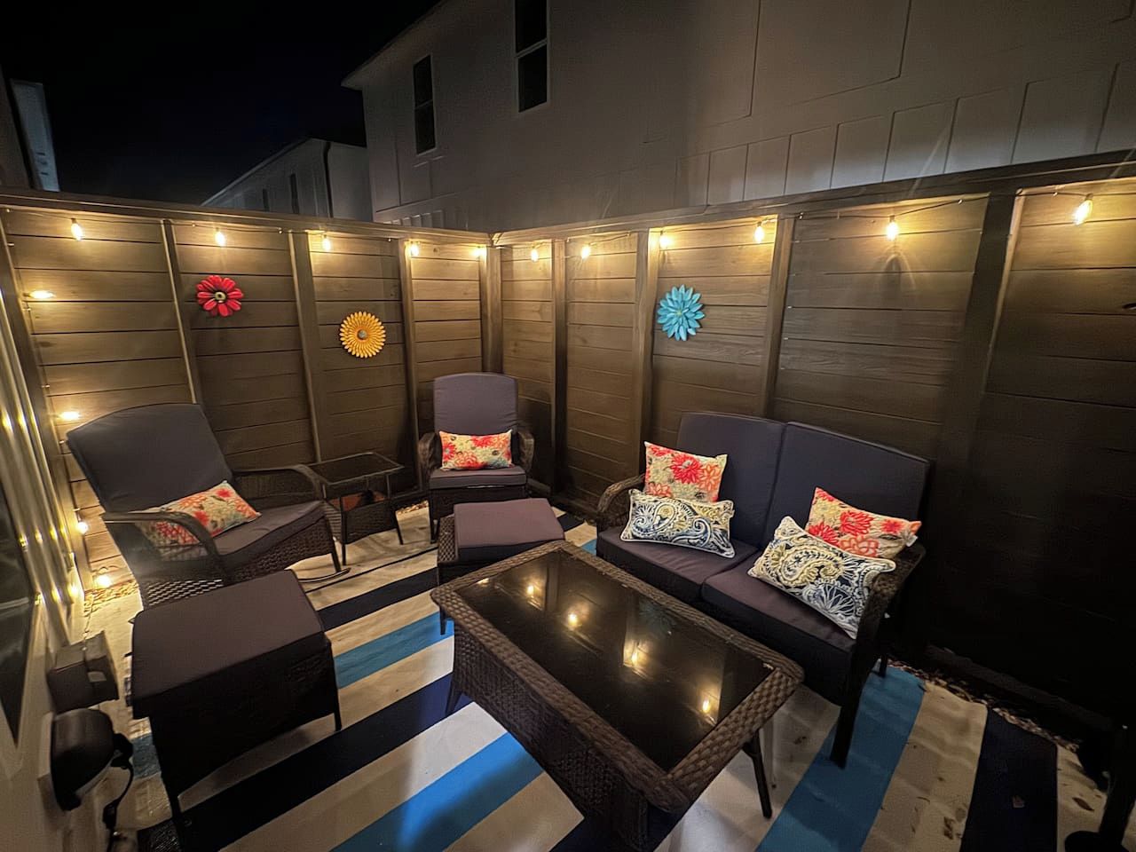 Une terrasse extérieure avec des murs en bois, des guirlandes lumineuses et du mobilier comprenant des chaises et un canapé.