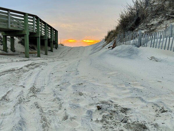 A sandy beach with a wooden boardwalk and a fence.