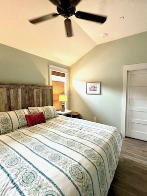 A bedroom with a bed, a ceiling fan, a nightstand, a lamp, and a door. - NEW! Prime Location @Beach Club -Tranquil Seascape (Corolla)