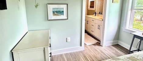 Un dormitorio con cama, cómoda, planta colgante y vista al baño.