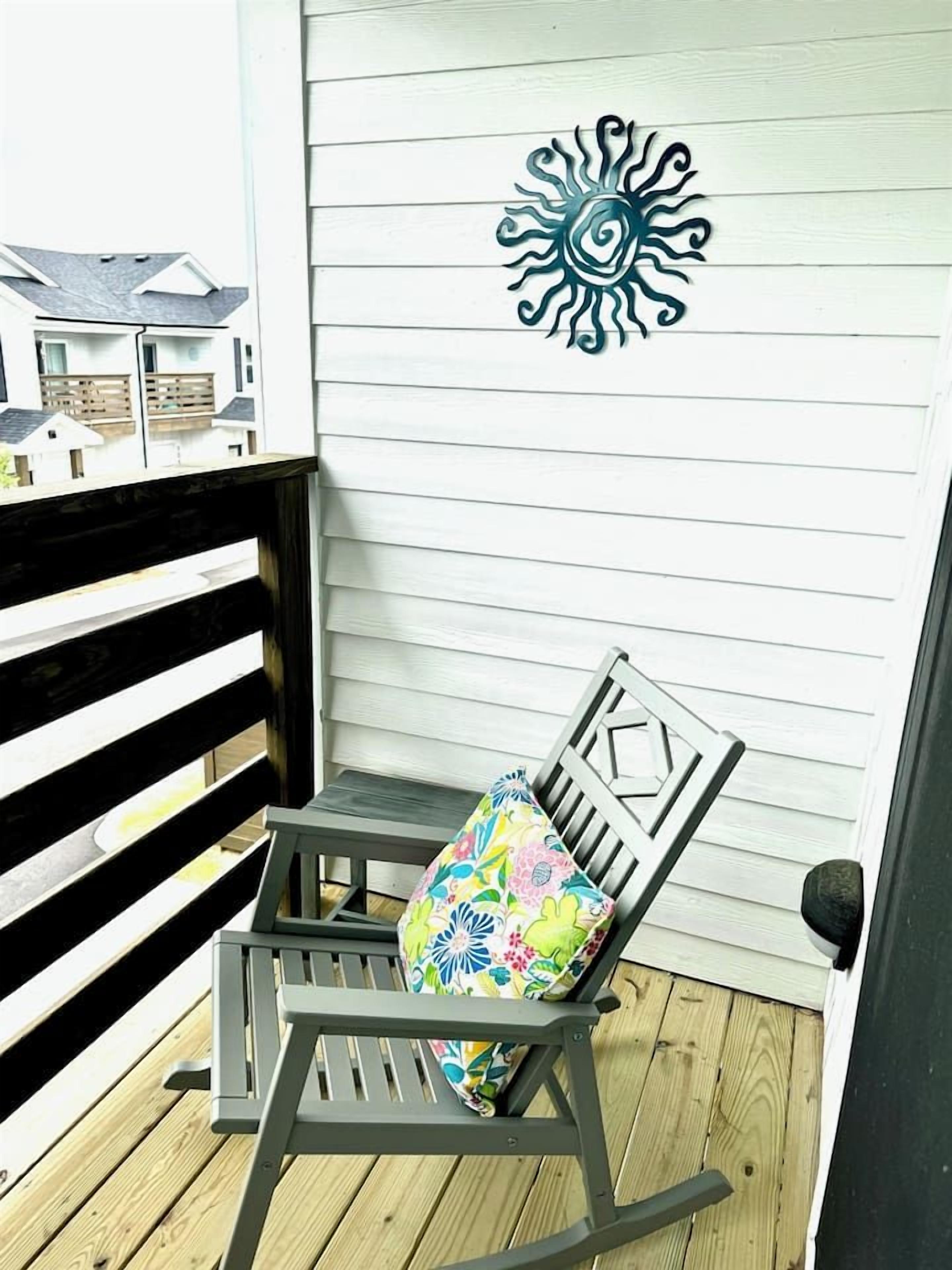 A wooden deck with a rocking chair and a colorful cushion.