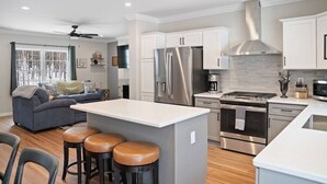 A modern kitchen with white cabinets, stainless steel appliances, and a central island with stools. - Built for You - 4BR w/ Playground, Sauna, Games! (Harbor Springs)