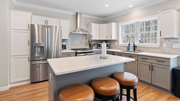A modern kitchen with white cabinets, stainless steel appliances, and a central island with stools. - Built for You - 4BR w/ Playground, Sauna, Games! (Harbor Springs)