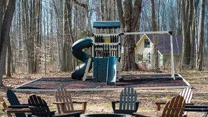 A playground with a slide and swings, surrounded by trees. - Built for You - 4BR w/ Playground, Sauna, Games! (Harbor Springs)