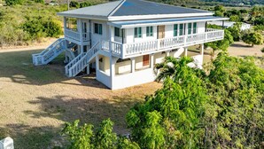 A white two-story house with a balcony, a staircase, and a view of the surrounding landscape.