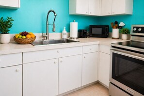 A kitchen with white cabinets, a stainless steel sink, a microwave, and an oven.