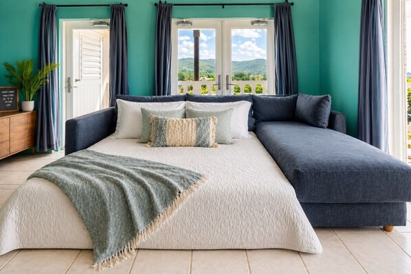 A bedroom with a bed, a sofa, a view of the outdoors, and a plant.