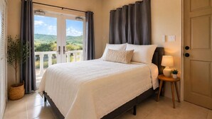 A bedroom with a bed, curtains, a nightstand with a lamp, a potted plant, and a view of greenery outside.